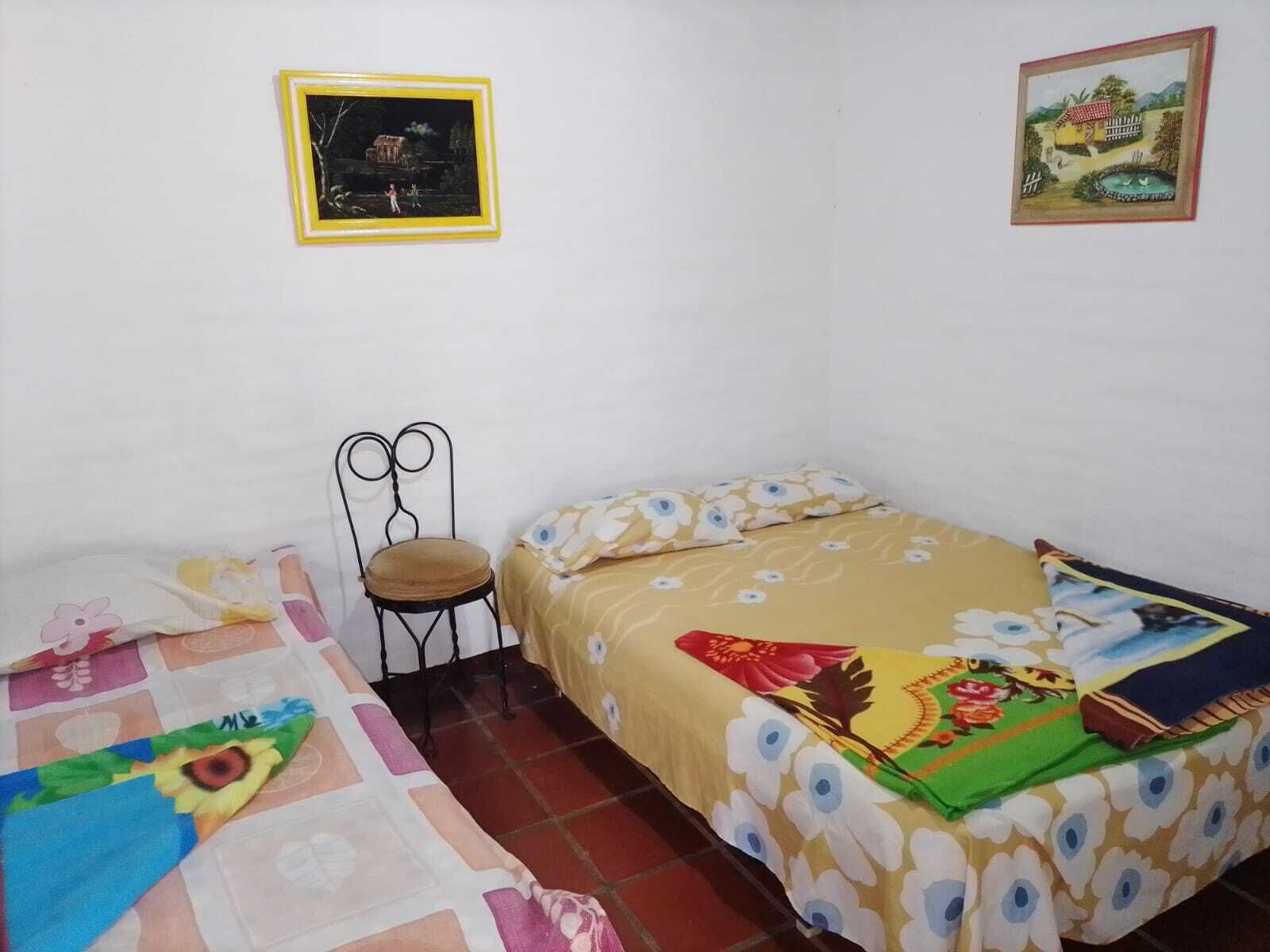 A bedroom with a bed, a chair, and two paintings on the wall.