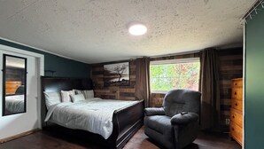 A bedroom with a bed, a chair, a dresser, a window with a view, and a mirror.