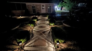 A pathway leading to a building with a number '7150' on the door, surrounded by well-lit garden lights and trimmed bushes.
