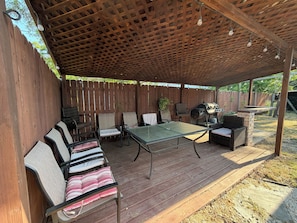 Eine überdachte Terrasse mit Tisch, Stühlen, einem Grill und einem Holzzaun.