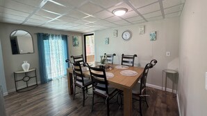 A dining area with a wooden table, black chairs, a mirror, a clock, and a window with curtains.