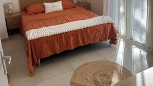 Een slaapkamer met een bed, nachtkastjes, een lamp, decoratieve wandkunst en uitzicht door dunne gordijnen.