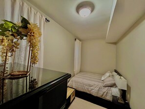 Ein Schlafzimmer mit einem Bett, einem Nachttisch, einer Lampe, einer Kommode und einer Zierpflanze.