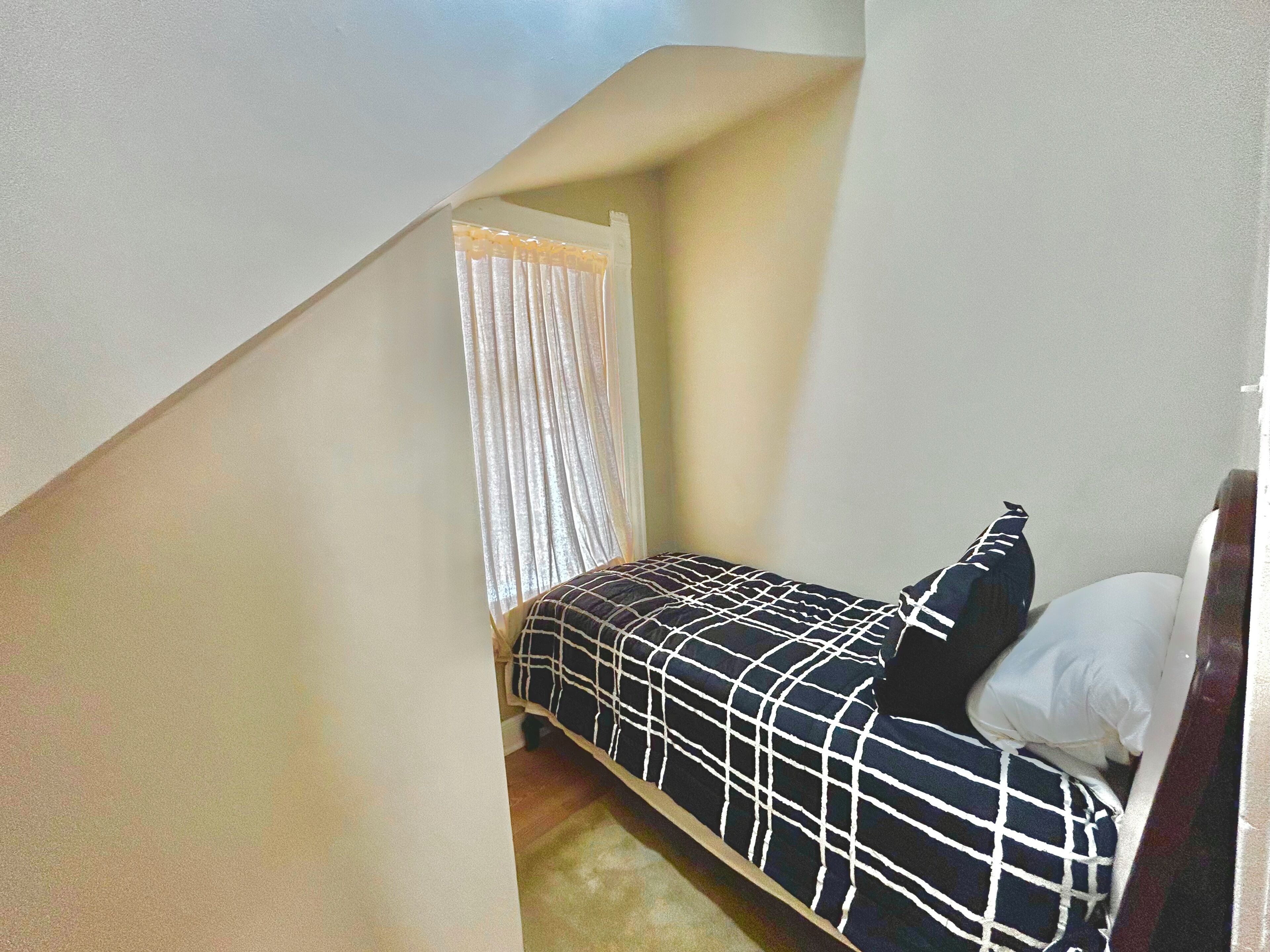 Un dormitorio con cama, ventana con cortinas y techo inclinado.