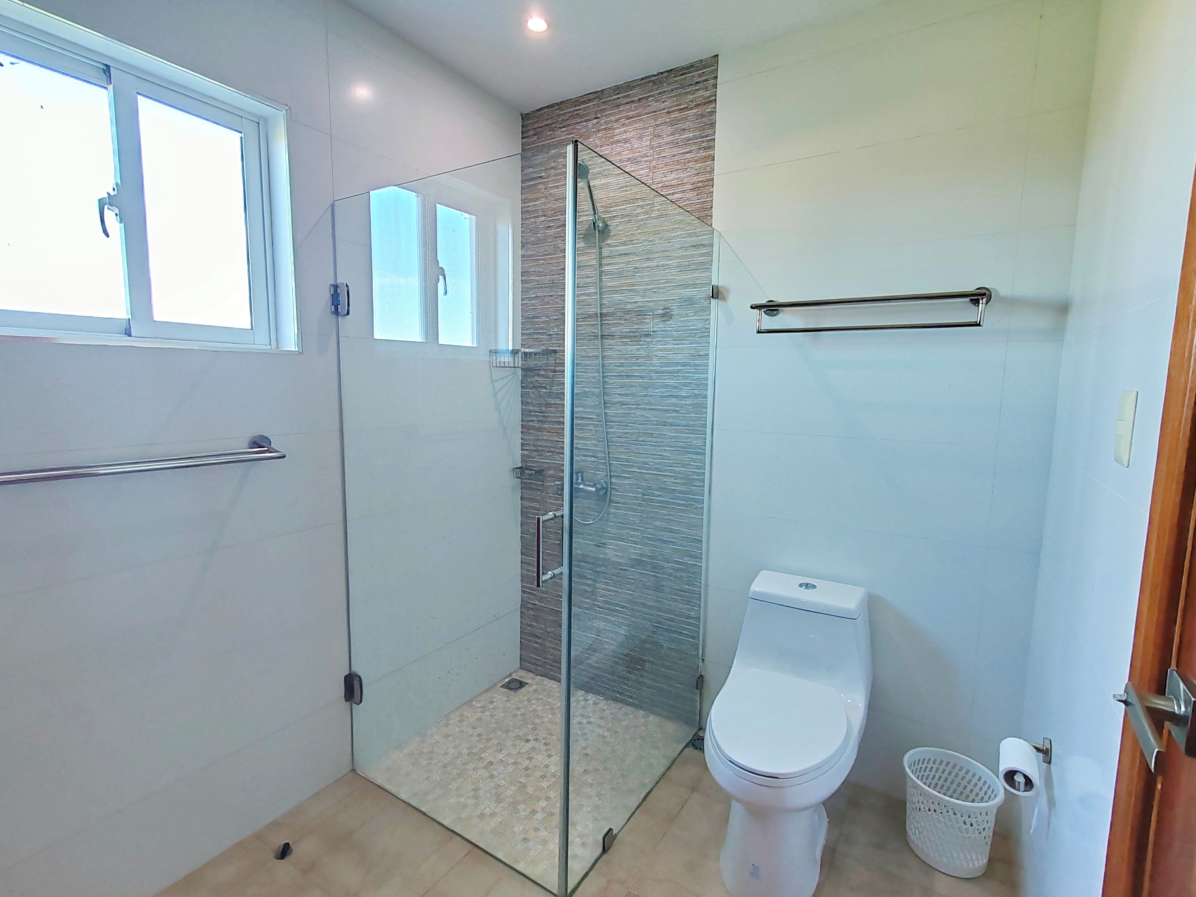 Ein modernes Badezimmer mit einer Duschkabine, einer Toilette und einer kleinen Mülltonne.