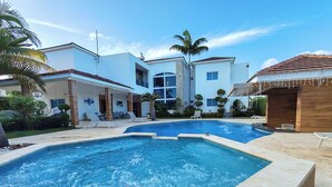 Una piscina con sillas de descanso, una estructura de madera y un edificio moderno con fachada de piedra.
