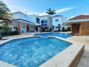 Ein Swimmingpool mit Liegestühlen, einer Holzkonstruktion und einem modernen Gebäude mit Natursteinfassade.