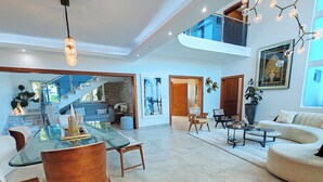Amplia sala de estar con mesa de comedor de vidrio, muebles modernos y una escalera que conduce a un nivel superior.