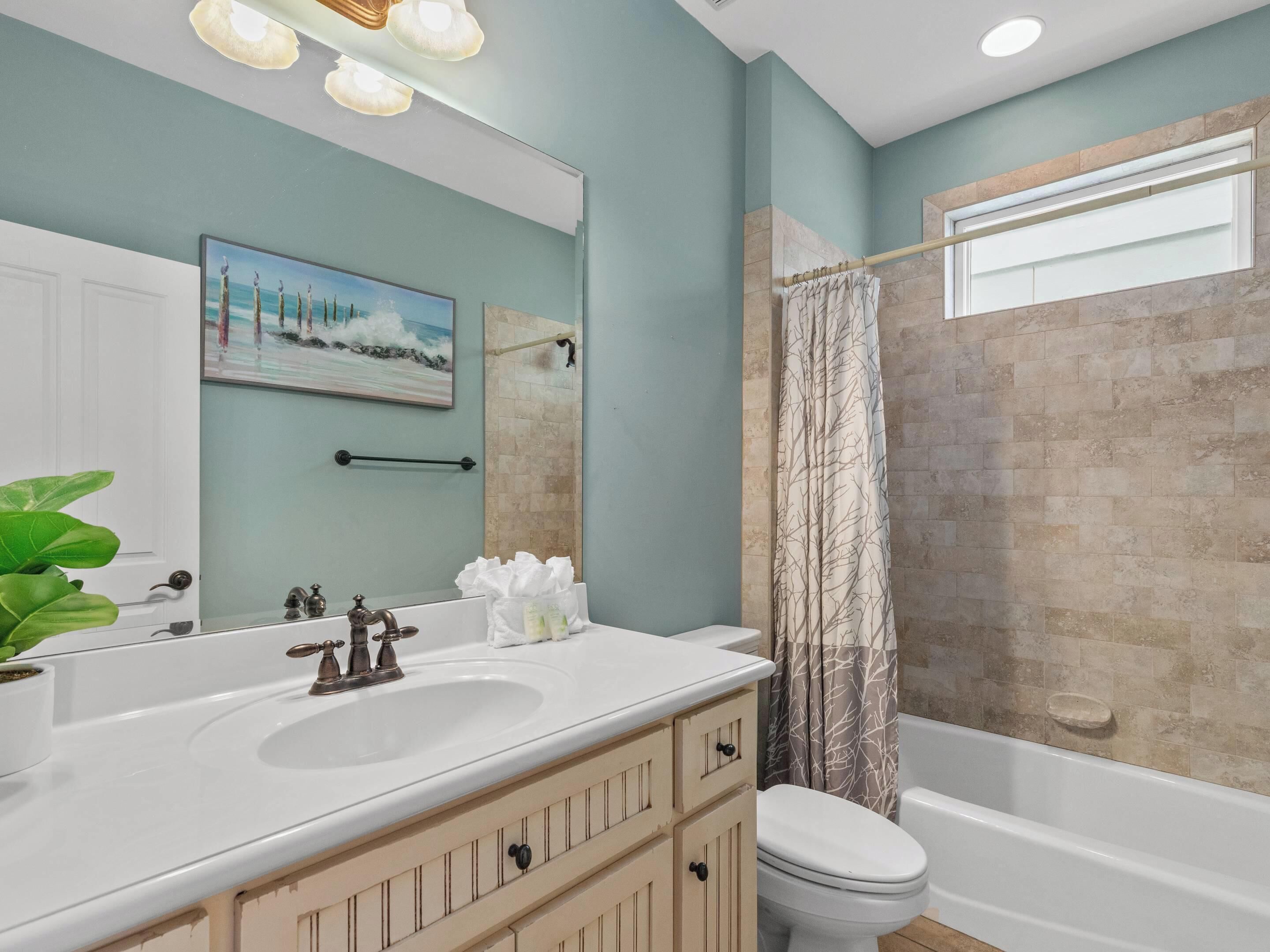 Une salle de bain avec un lavabo blanc, deux robinets, un miroir, des toilettes et un rideau de douche.