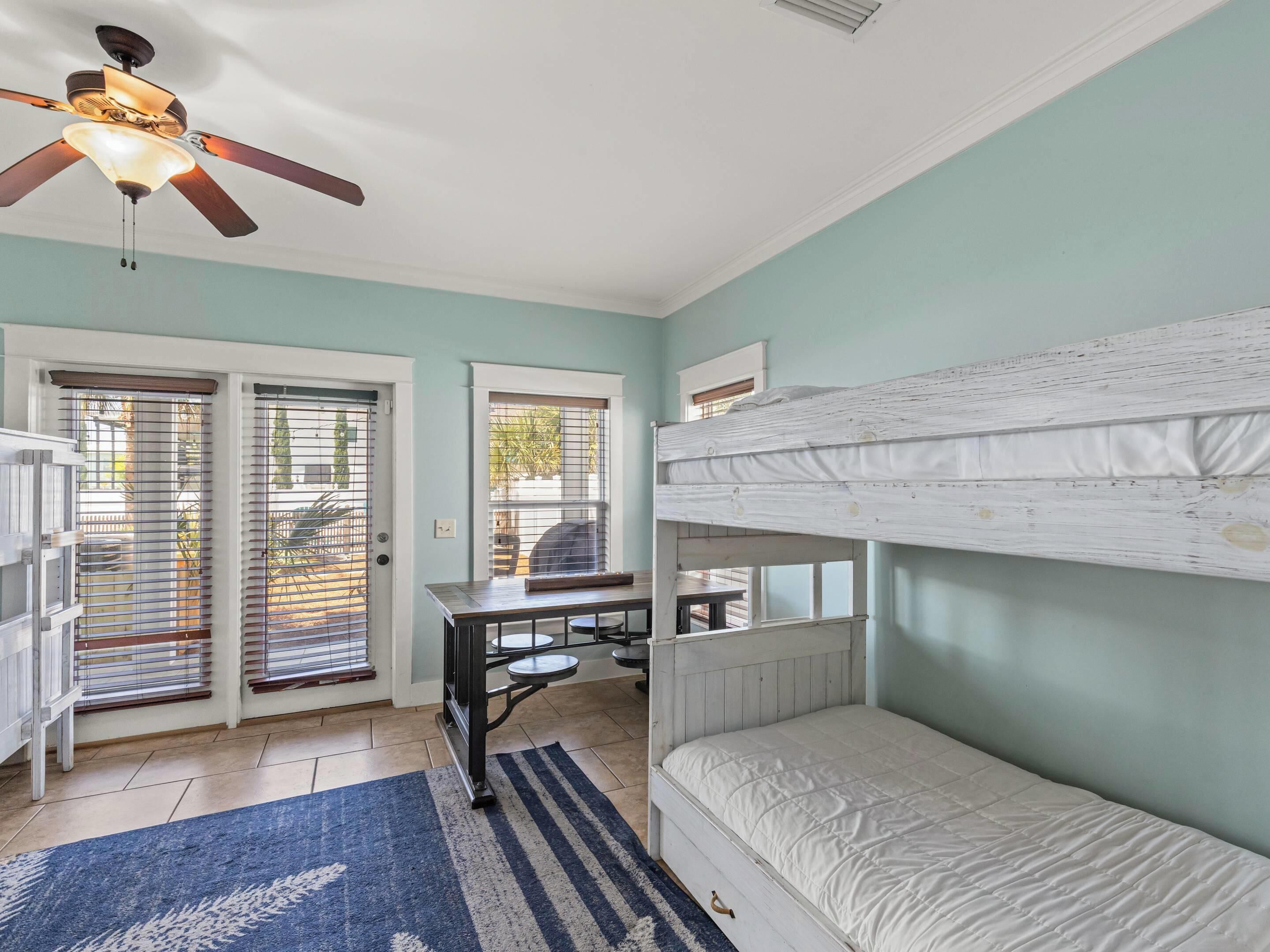 A room with a ceiling fan, bunk beds, a desk, and a window with blinds.