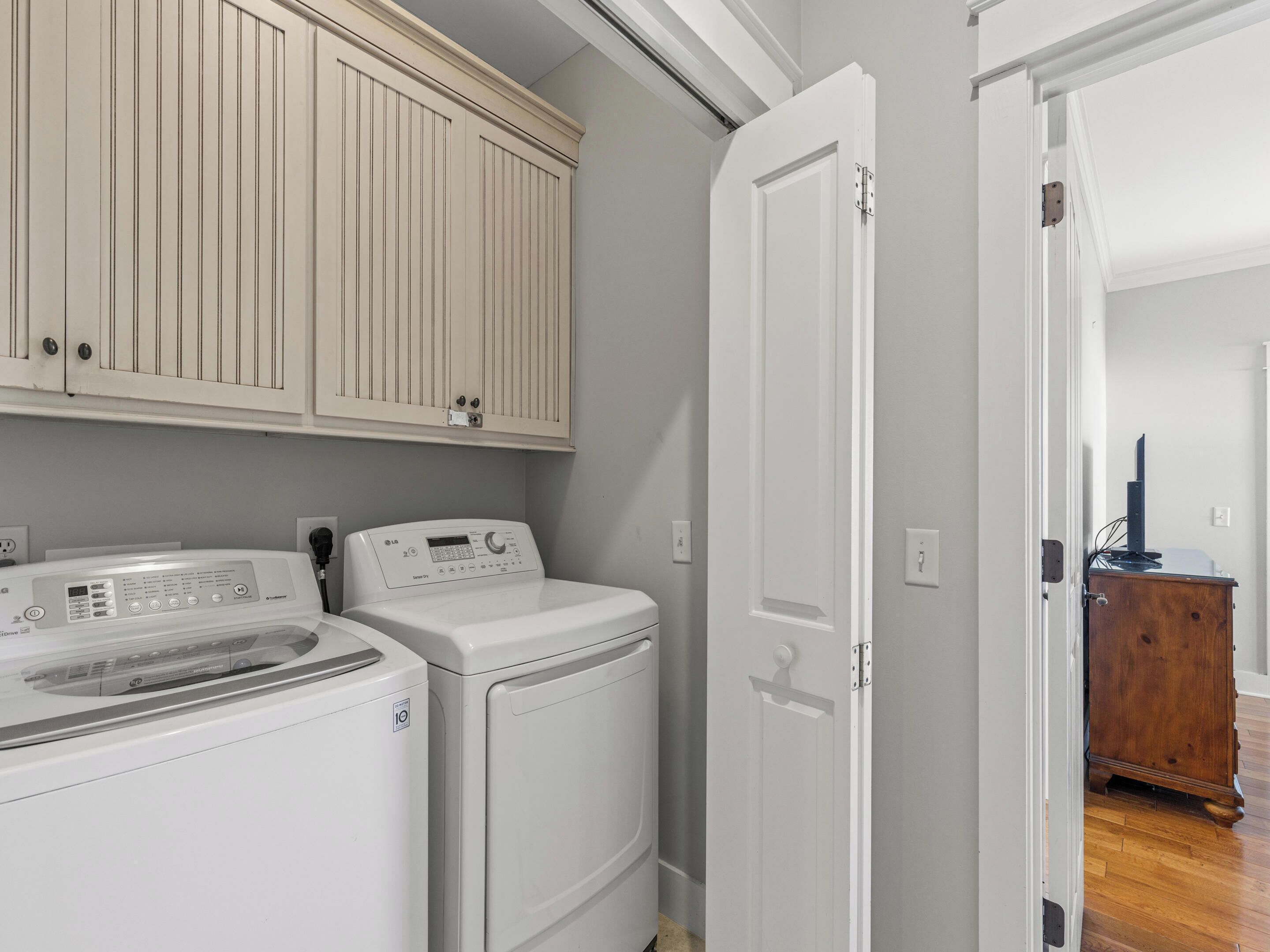 Een wasruimte met een voorlader wasmachine en droger, houten kastjes erboven, en een deur naar een andere kamer.
