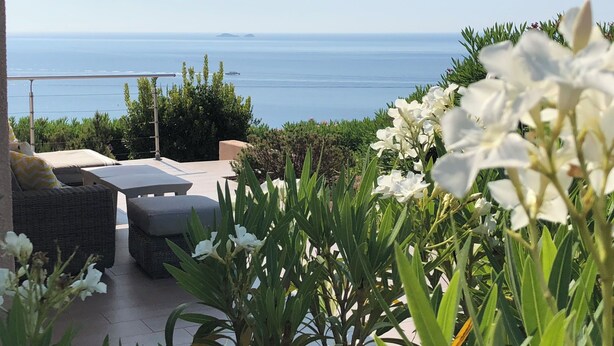 Un patio con mobiliario exterior, vista al mar y flores blancas al frente.