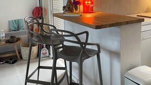 Una cocina moderna con encimera de madera, dos taburetes de bar, una pequeña mesa de comedor y una lámpara colgante.