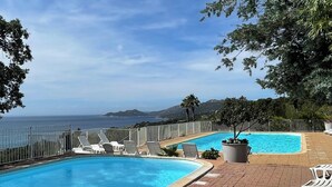 Una piscina con vista al océano, rodeada de sillas de descanso y un patio de ladrillo.