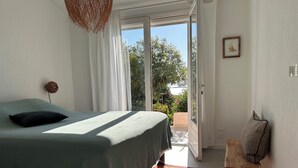 Un dormitorio con cama, una lámpara colgante, una puerta que da a un balcón y un taburete de madera.