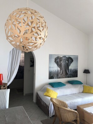 A modern bedroom with a white bed, teal and yellow pillows, a wooden hanging light fixture, a framed elephant picture, and a wicker chair. - Rental mini villa 180° sea view Palombaggia Porto Vecchio (Porto-Vecchio)