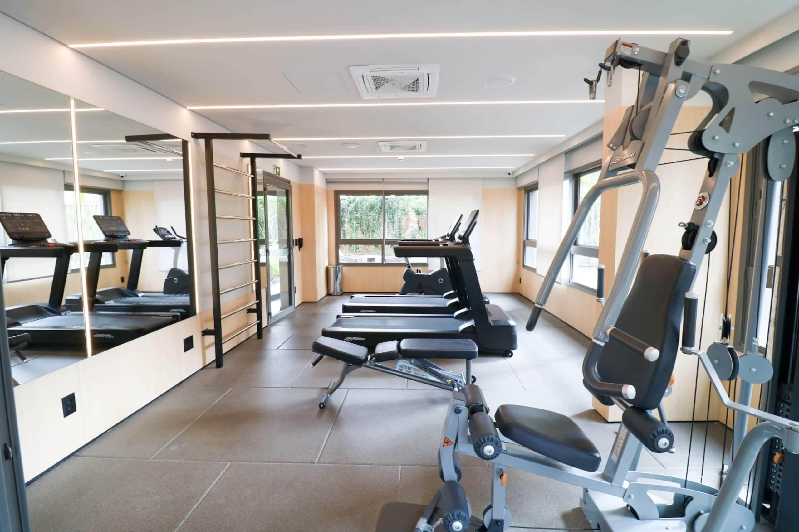Ein Fitnessstudio mit Laufbändern, Kraftgeräten und einer Spiegelwand.