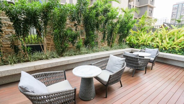 A rooftop patio with wicker furniture, a round table, and lush greenery. - Studio Moderno GO Balkon Campo Belo - SP (São Paulo)