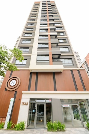 Um edifício alto com design moderno, apresentando uma entrada destacada com portas de vidro, o número do endereço visível e um logotipo na fachada.