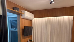 A bedroom with a bed, a TV mounted on the wall, a bedside table with a phone, and a window with curtains. - Studio Moderno GO Balkon Campo Belo - SP (São Paulo)