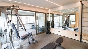 A modern gym with exercise equipment, a bench, and a mirror reflecting the space. - Studio Moderno GO Balkon Campo Belo - SP (São Paulo)