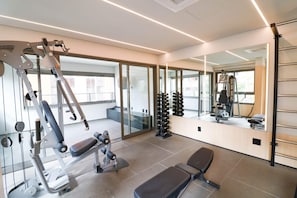 Academia moderna com equipamentos de exercício, um banco e um espelho refletindo o espaço.