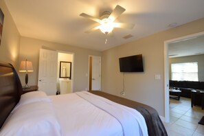 Ein Hotelzimmer mit einem Bett, einem Deckenventilator, einem Fernseher und einer Tür zu einem Wohnbereich.