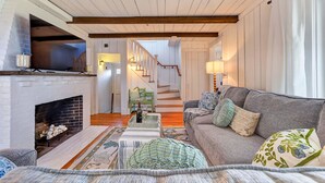 A cozy living room with a fireplace, a sofa, a staircase, and a dining area. - Steps To Peggotty Beach! Slps 10 + Dogs OK! (Scituate)