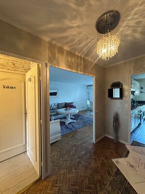 A hallway with a herringbone floor, a chandelier, a door labeled 'Toilets,' and a glimpse of a living room with a sofa and a table. - Apartment near the airport, CAP 3000 and the beaches (Saint-Laurent-du-Var)