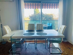 A dining area with a white table, four chairs, and a view of a balcony with outdoor furniture. - Apartment near the airport, CAP 3000 and the beaches (Saint-Laurent-du-Var)