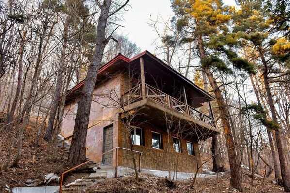 Une cabane à deux étages dotée d’un balcon, entourée d’arbres.