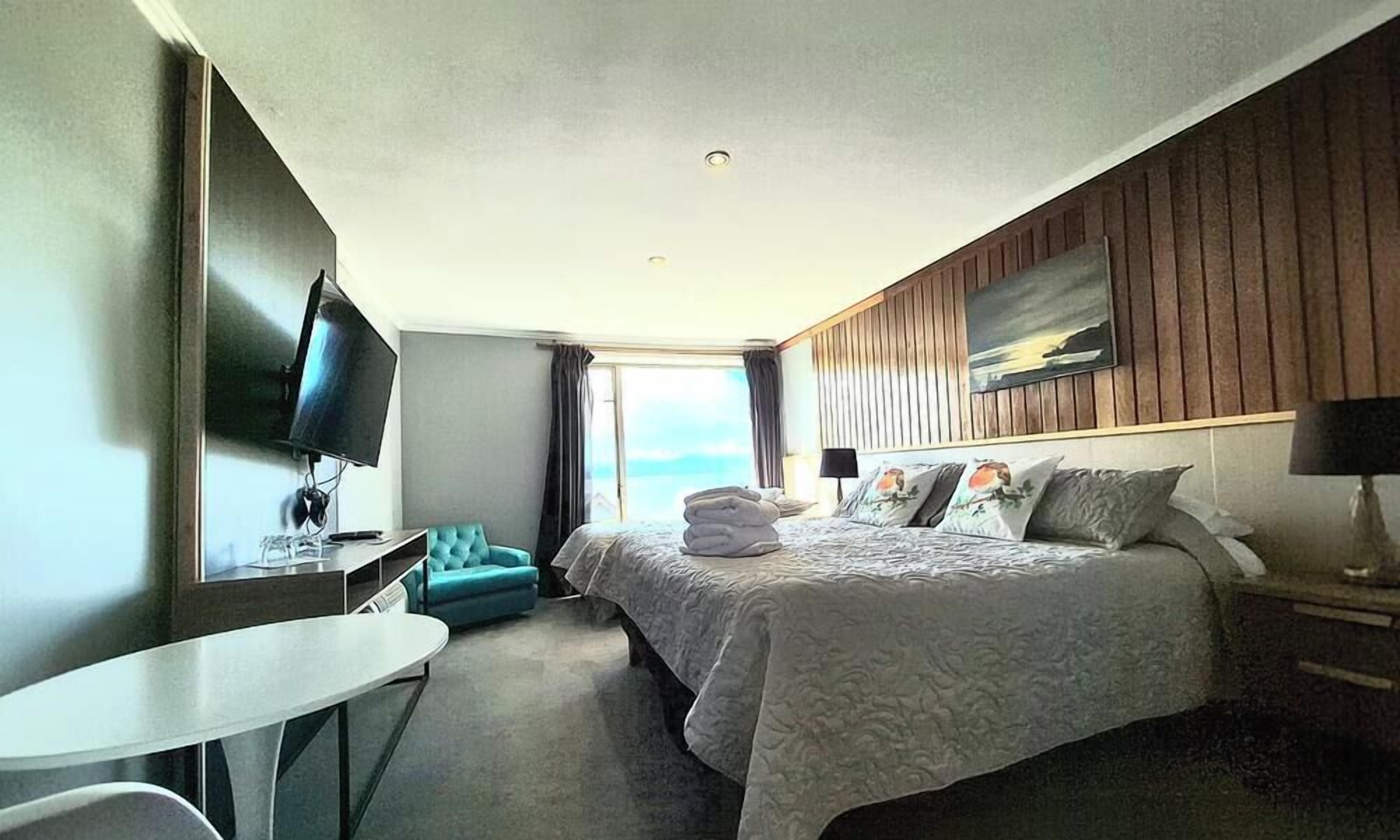A hotel room with a bed, a desk, a TV, and a view of the ocean.
