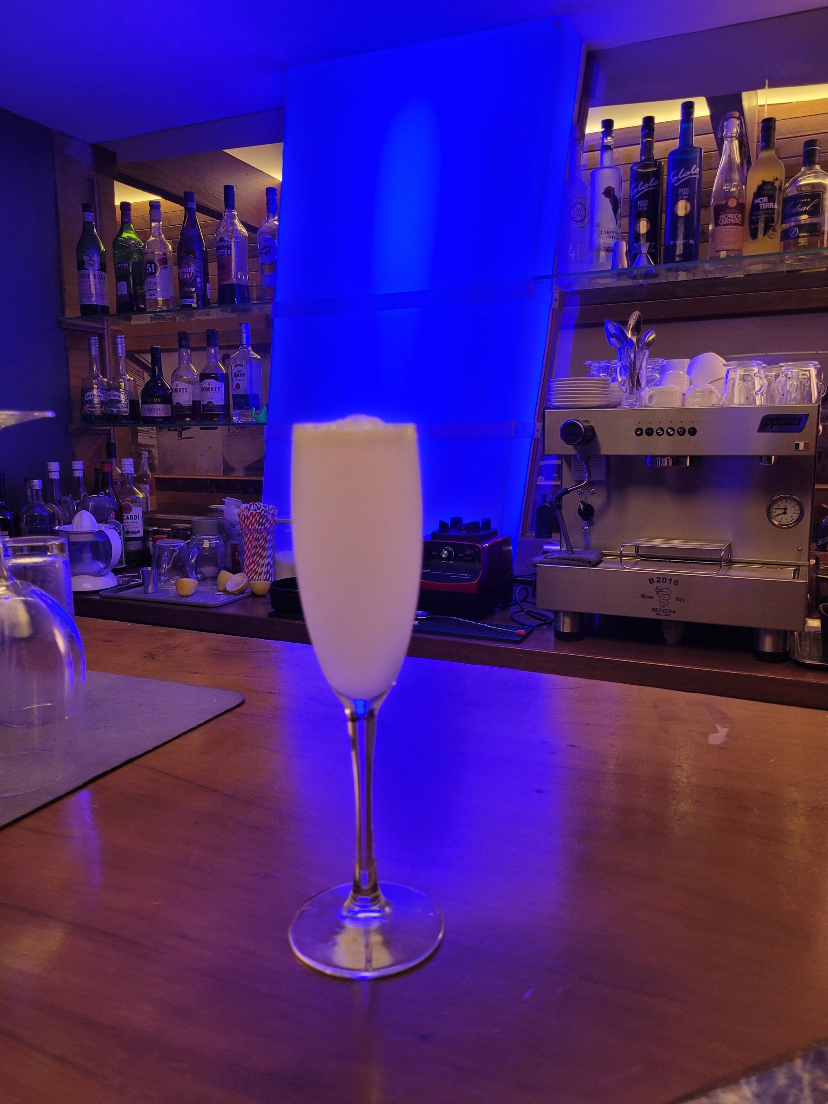 A bar area with a glass of white beverage, shelves of liquor bottles, and a coffee machine.