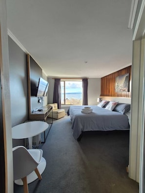 Una habitación de hotel con una cama, un escritorio con una silla, una mesita y un televisor.
