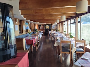 Un restaurante con suelos de madera, mesas dispuestas con manteles blancos y grandes ventanales.