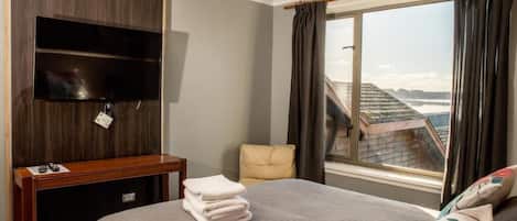Habitación de hotel con cama, televisor montado en la pared, ventana con cortinas y vistas al exterior.