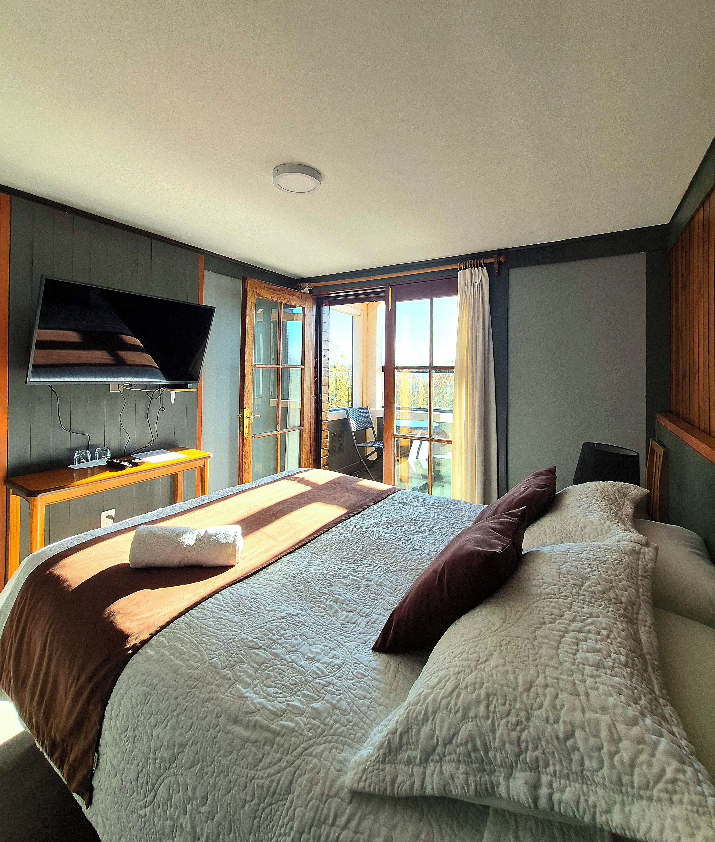 Ein Hotelzimmer mit Bett, Fernseher, Schreibtisch mit Stuhl und Balkon mit Blick.