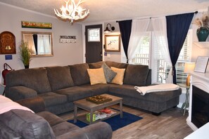 Ein Wohnzimmer mit einem Ecksofa, einem Couchtisch, einem Kamin und einer Deckenleuchte.