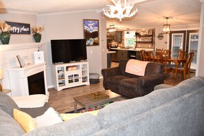 Ein Wohnzimmer mit Kamin, Fernseher, einer Couch und einem Essbereich mit Stühlen und einem Tisch.