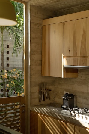 A kitchen with wooden cabinets, a gas stove, and a window with a view of greenery. - Casa Macu Saladita Surf House (Ixtapa)