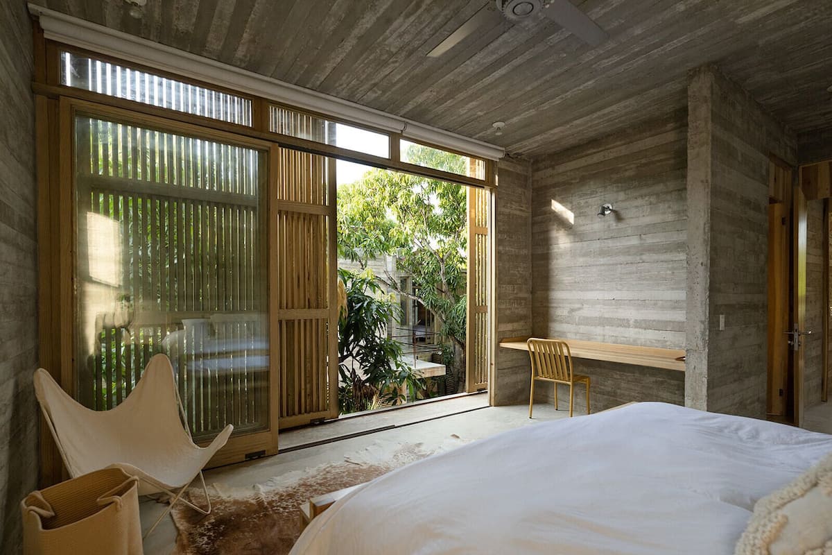 Quarto com cama, cadeira, escrivaninha e porta de correr para um jardim.