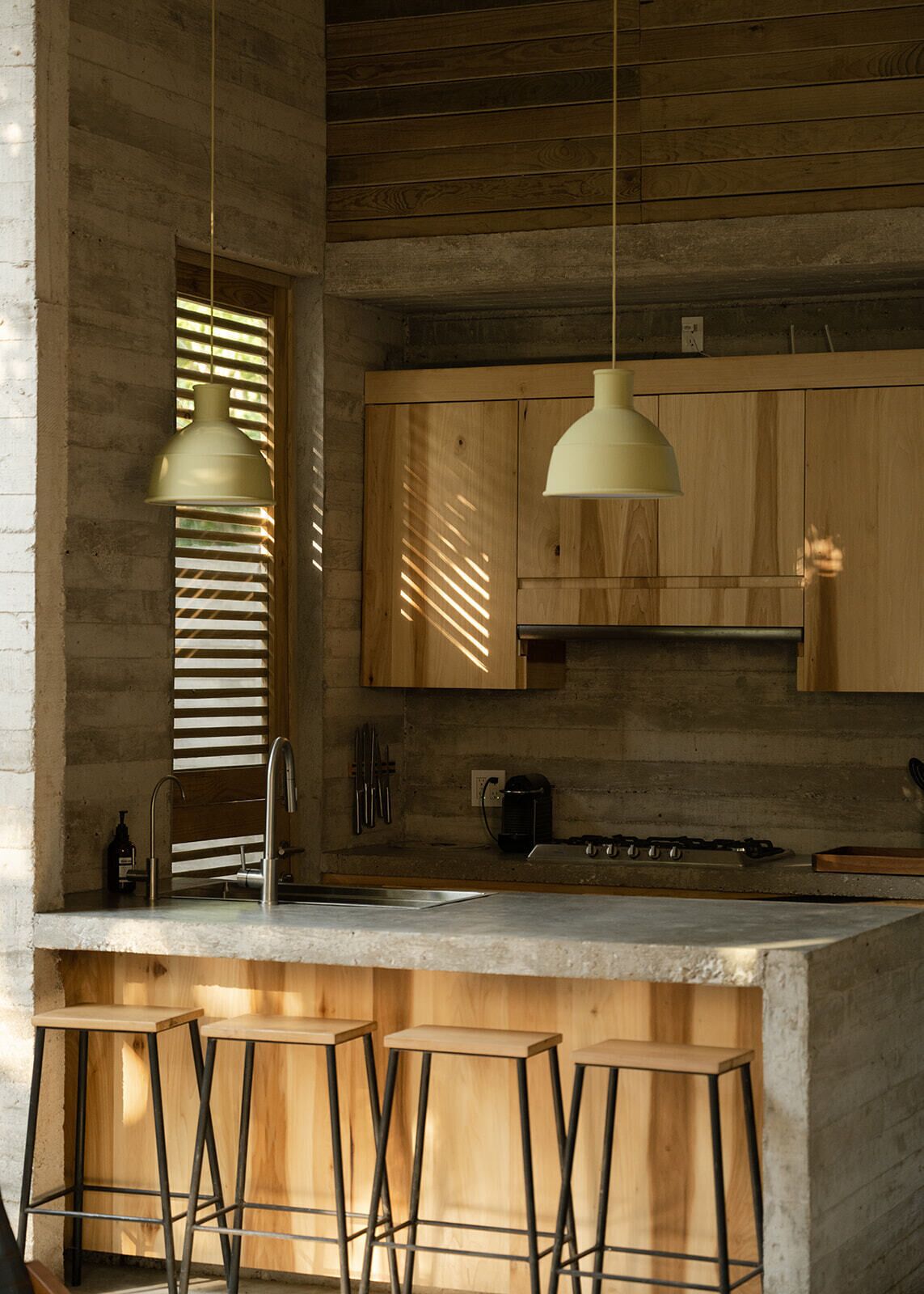 A modern kitchen with wooden cabinets, a bar area with stools, and pendant lighting.