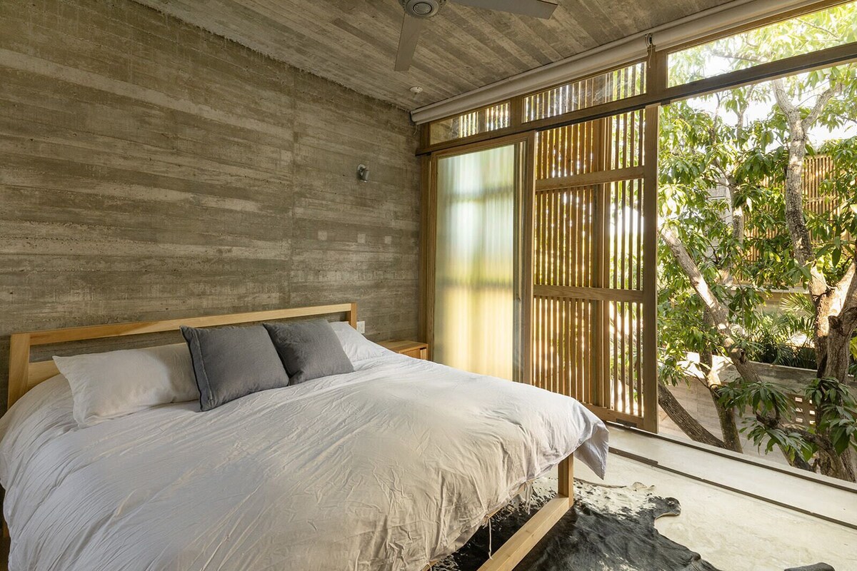 Un dormitorio con una cama grande, una pared de concreto y vistas a zonas verdes.