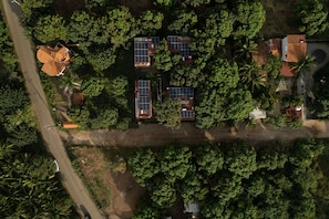An aerial view of a residential area with multiple houses, some with solar panels, surrounded by dense greenery and a road. - Casa Macu Saladita Surf House (Ixtapa)