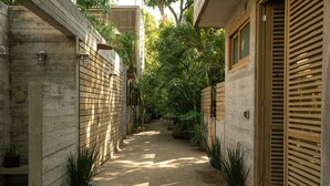 Un sendero estrecho bordeado por paredes de madera y plantas en macetas, que conduce a un edificio con puerta de madera.