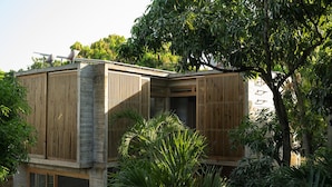 Un edificio moderno con listones verticales de madera, fachada de hormigón y abundante vegetación.