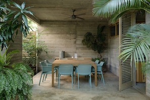 A concrete room with a ceiling fan, a wooden table, and four chairs. - Casa Macu Saladita Surf House (Ixtapa)