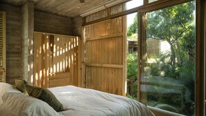 Un dormitorio con cama, armario de madera y puerta corrediza de vidrio que da a un jardín.
