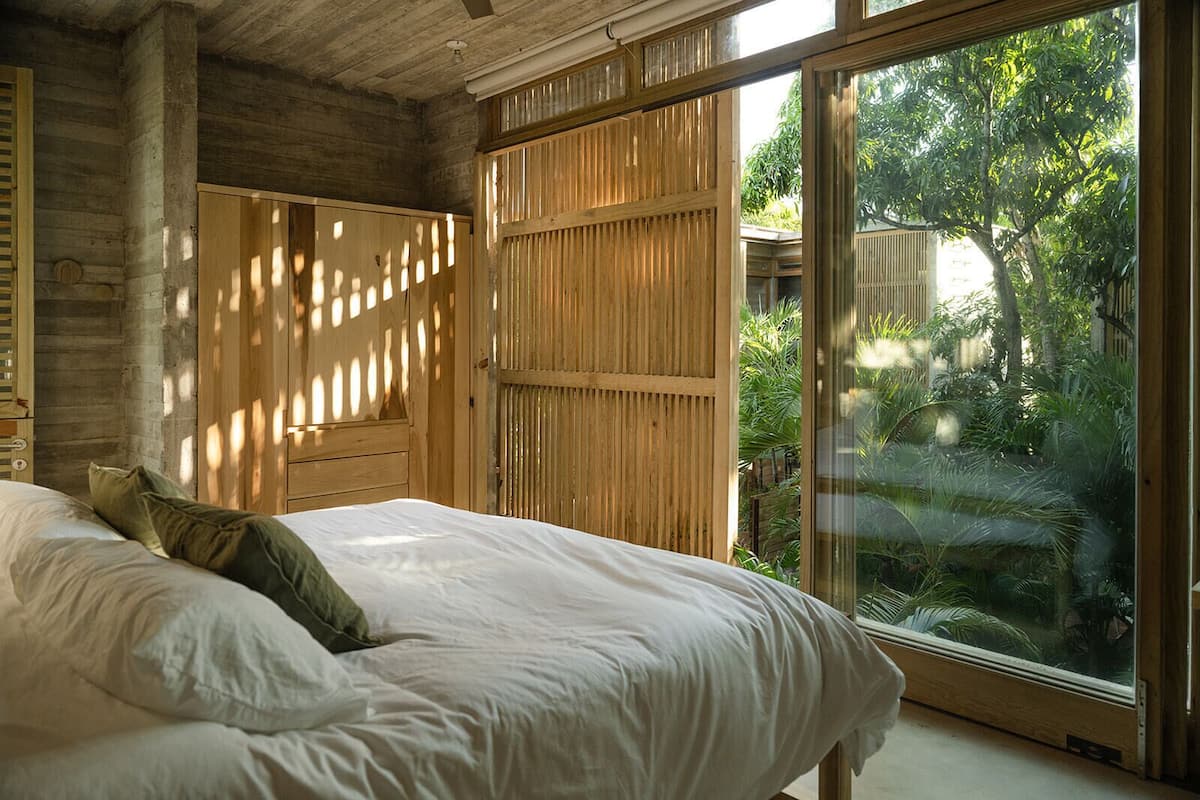 Quarto com cama, guarda-roupa de madeira e porta de vidro deslizante para um jardim.