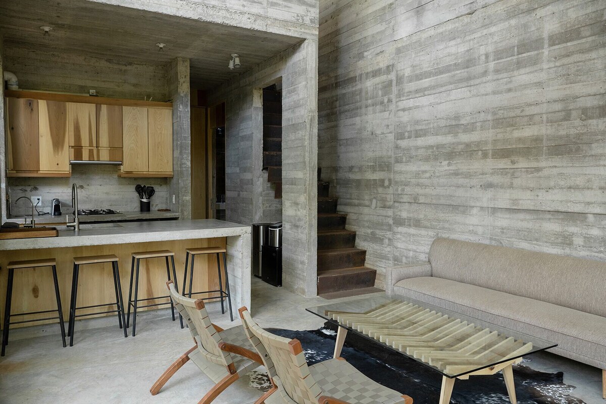 Una cocina moderna con armarios de madera, una zona con taburetes de bar y una escalera que sube a otro nivel.